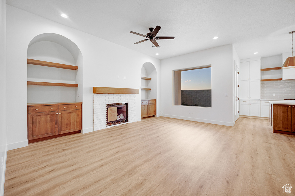 Unfurnished living room featuring ceiling fan, a brick fireplace, light hardwood / wood-style flooring, and built in shelves