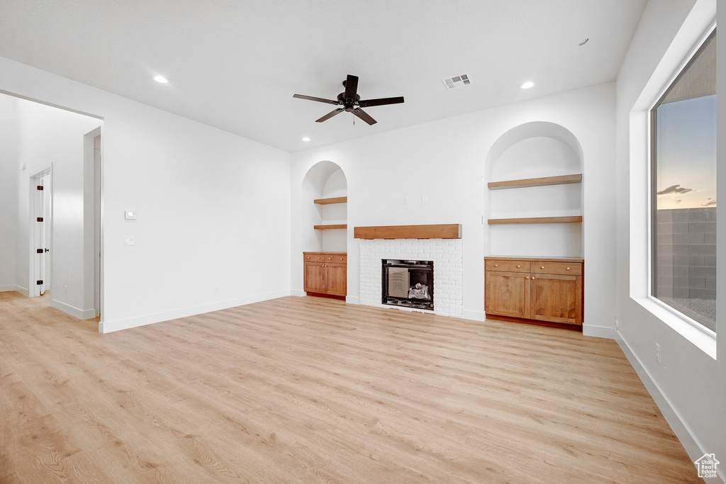Unfurnished living room featuring light hardwood / wood-style floors, ceiling fan, built in shelves, and a brick fireplace