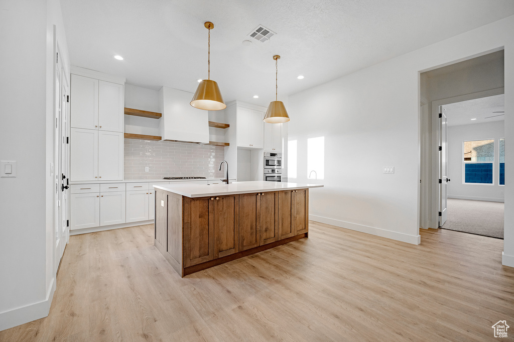 Kitchen with white cabinets, light hardwood / wood-style flooring, and a kitchen island with sink