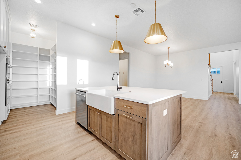 Kitchen with an island with sink, light hardwood / wood-style floors, and decorative light fixtures