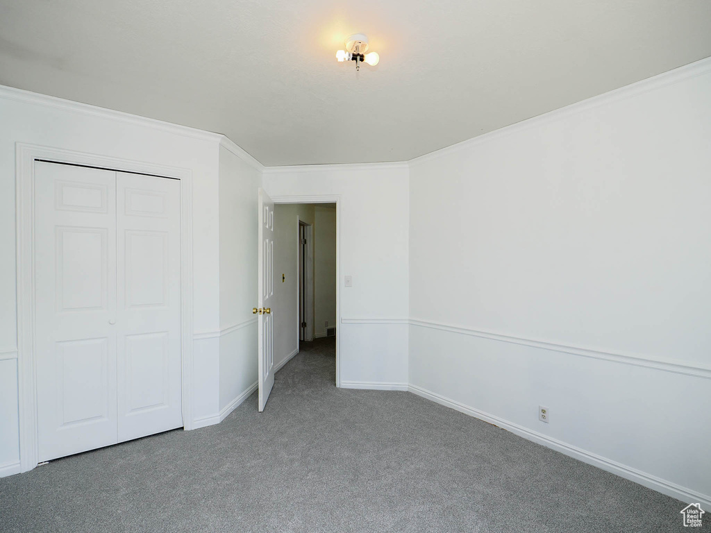 Unfurnished bedroom featuring a closet, dark carpet, and crown molding