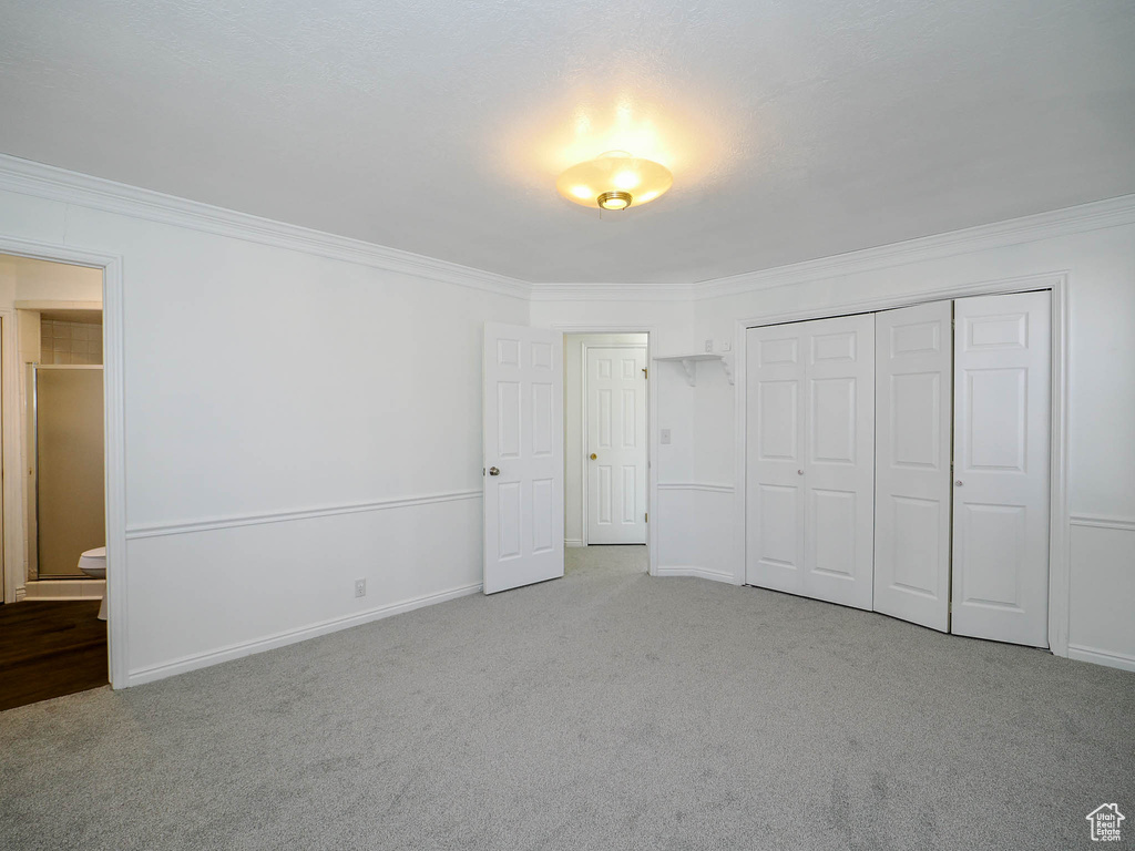 Unfurnished bedroom with light colored carpet, ensuite bath, and ornamental molding