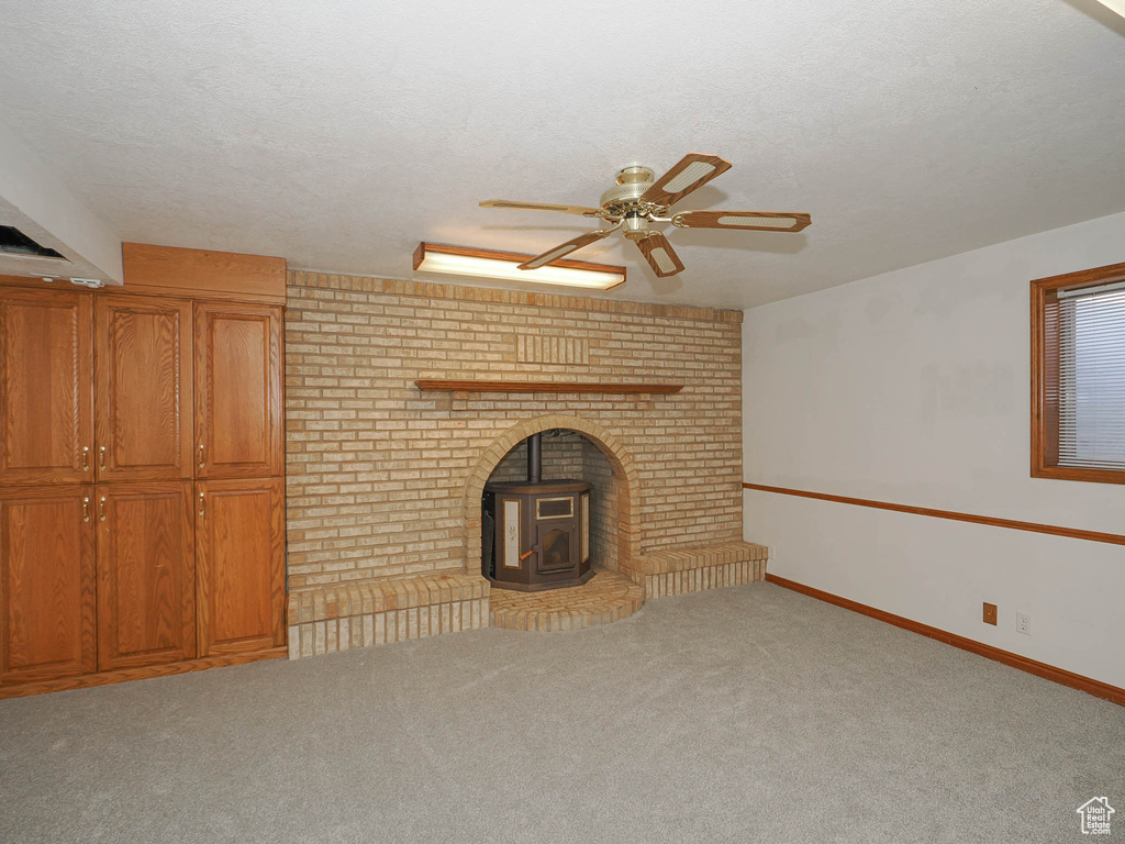 Unfurnished living room with light carpet, ceiling fan, a wood stove, and a textured ceiling