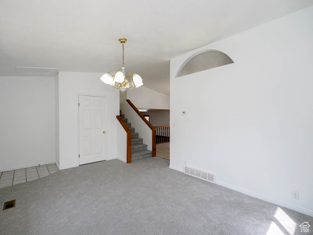 Carpeted empty room featuring a chandelier and lofted ceiling