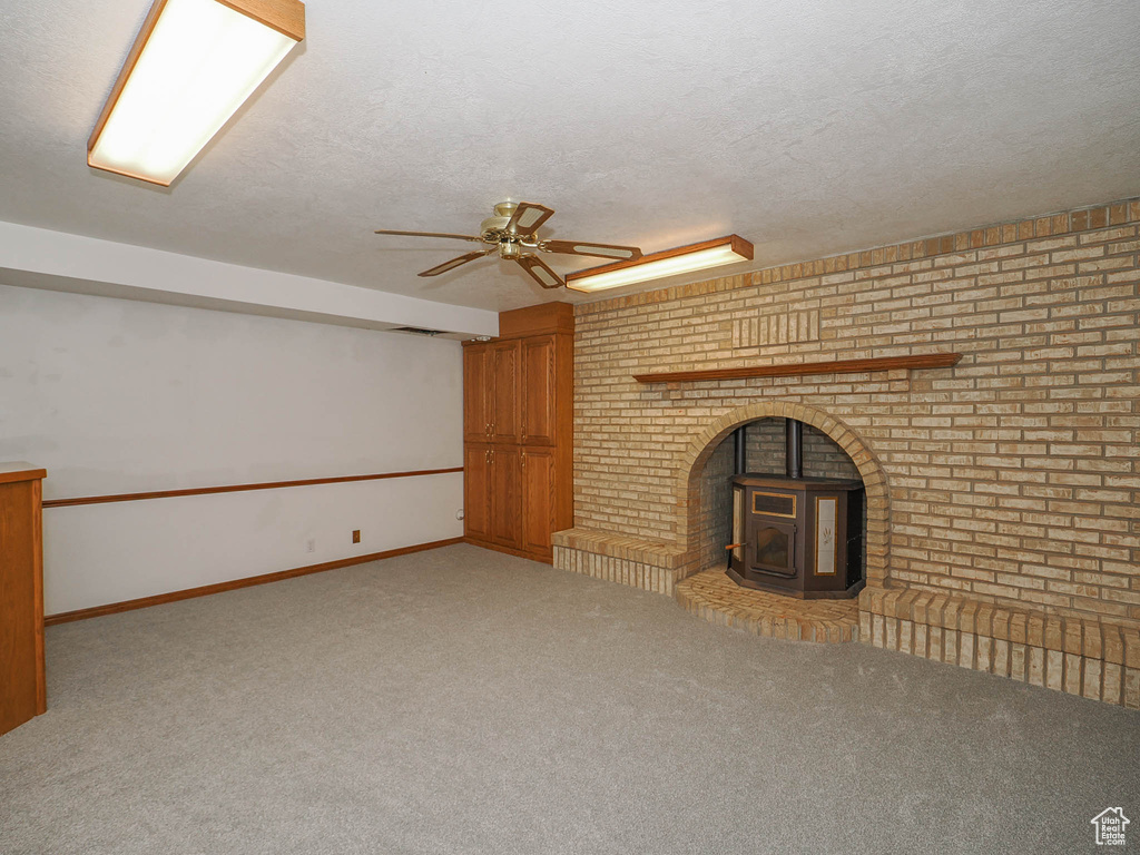 Unfurnished living room featuring light colored carpet, a wood stove, and ceiling fan