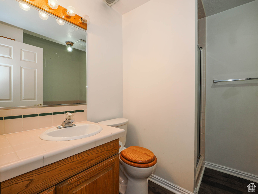 Bathroom featuring walk in shower, hardwood / wood-style floors, vanity, and toilet