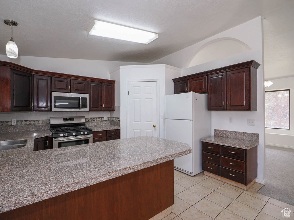 Kitchen with appliances with stainless steel finishes, backsplash, light tile floors, and decorative light fixtures