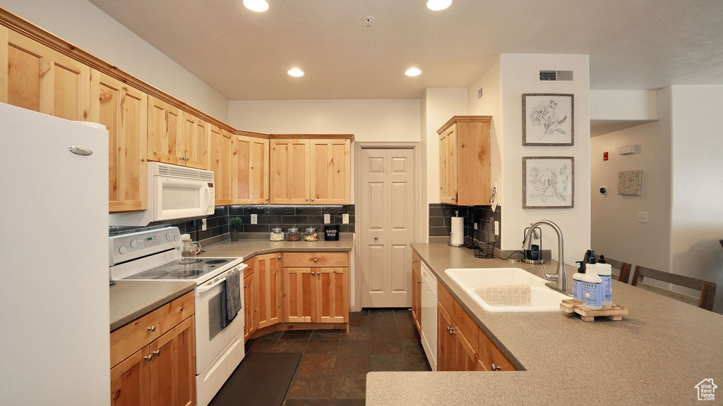 Kitchen featuring sink, backsplash, dark tile flooring, and white appliances