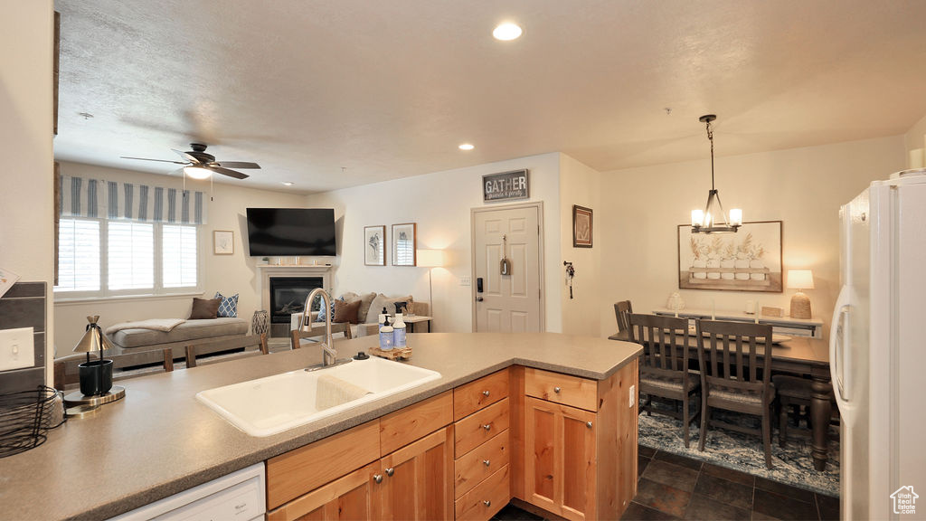Kitchen featuring dark tile floors, pendant lighting, white appliances, ceiling fan with notable chandelier, and sink