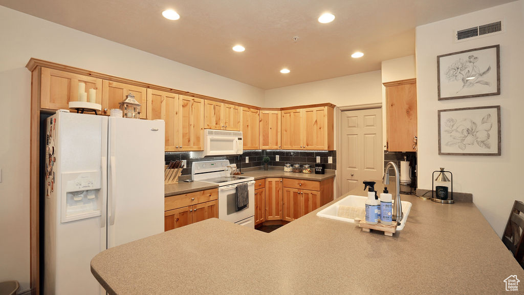 Kitchen with light brown cabinetry, kitchen peninsula, backsplash, white appliances, and sink