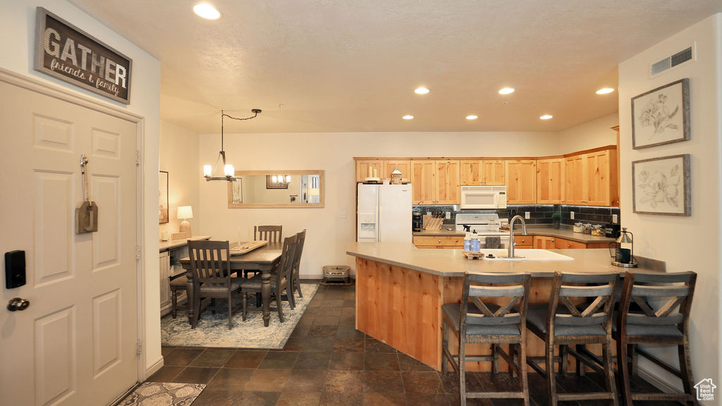 Kitchen featuring decorative light fixtures, sink, light brown cabinetry, white appliances, and dark tile flooring