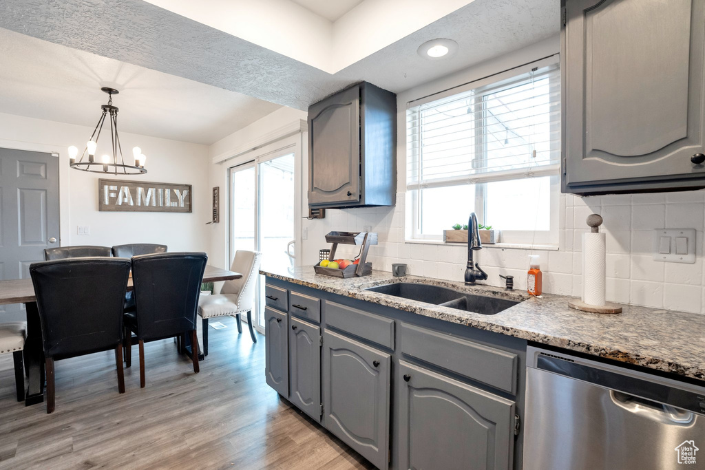 Kitchen featuring backsplash, decorative light fixtures, dishwasher, a chandelier, and light hardwood / wood-style flooring