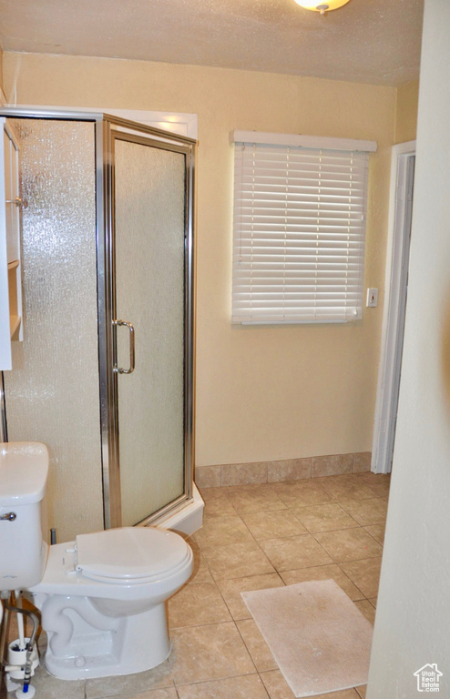 Bathroom with tile flooring, toilet, and a shower with shower door