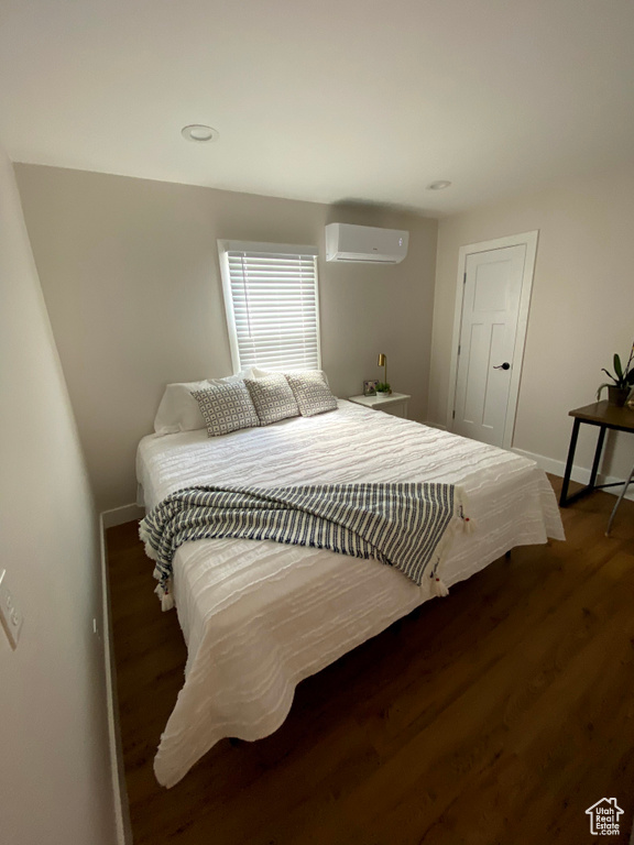 Bedroom with a wall mounted air conditioner and dark hardwood / wood-style floors
