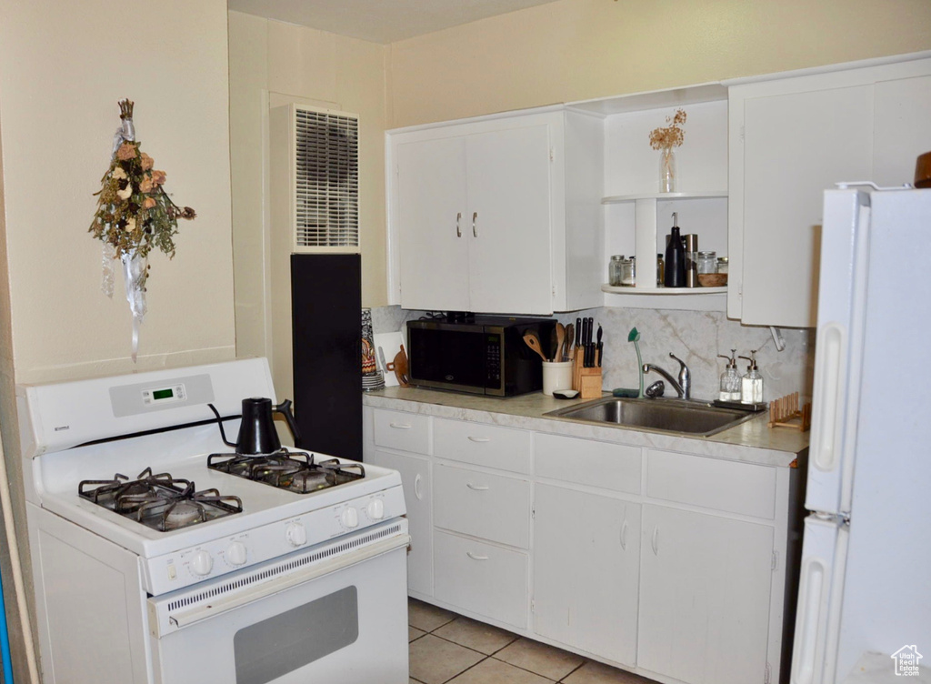 Kitchen with light tile flooring, white cabinets, white appliances, and sink