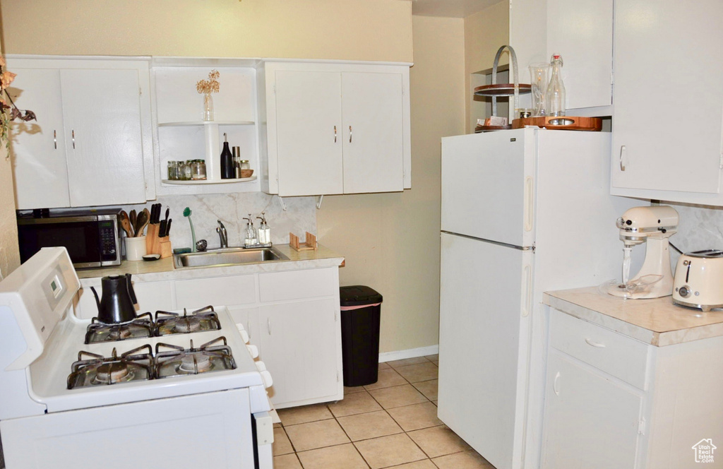 Kitchen with tasteful backsplash, light tile floors, white cabinetry, sink, and white stove