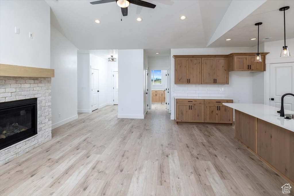 Kitchen with pendant lighting, light wood-type flooring, tasteful backsplash, ceiling fan, and a brick fireplace