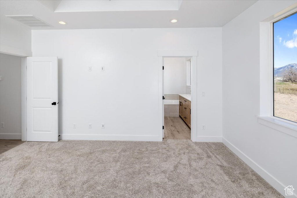 Unfurnished bedroom with multiple windows, connected bathroom, and light carpet