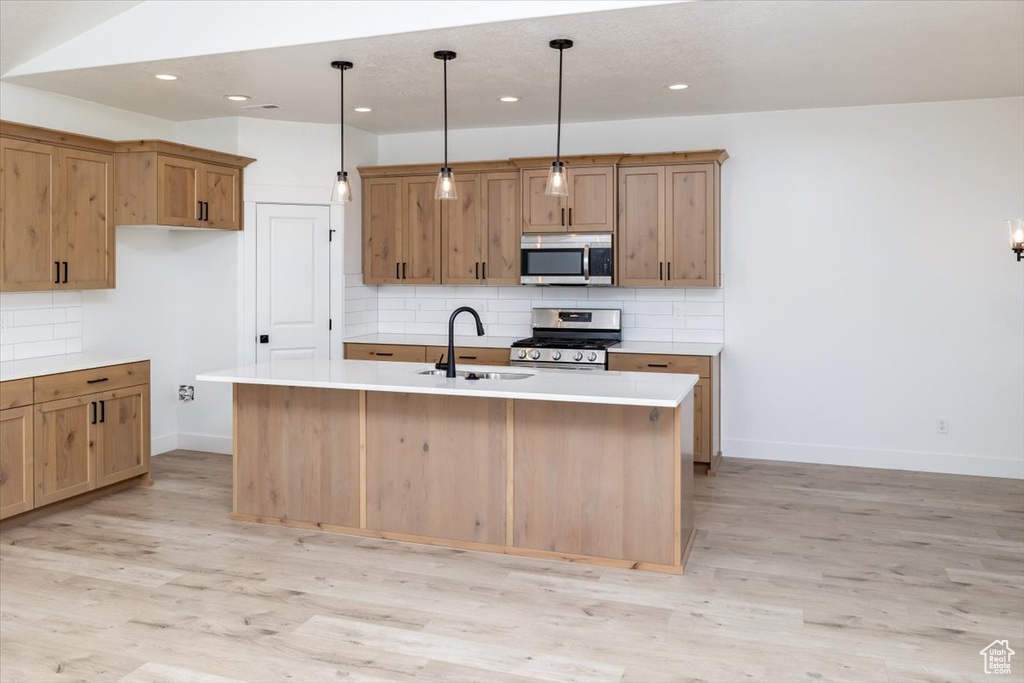Kitchen featuring decorative light fixtures, a center island with sink, light hardwood / wood-style flooring, appliances with stainless steel finishes, and backsplash