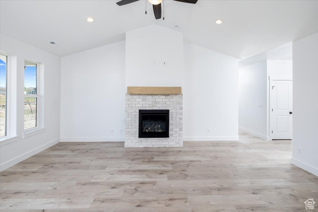 Unfurnished living room with a brick fireplace, light wood-type flooring, ceiling fan, and lofted ceiling