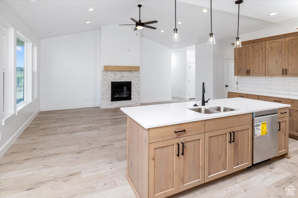 Kitchen featuring ceiling fan, sink, dishwasher, a center island with sink, and a fireplace
