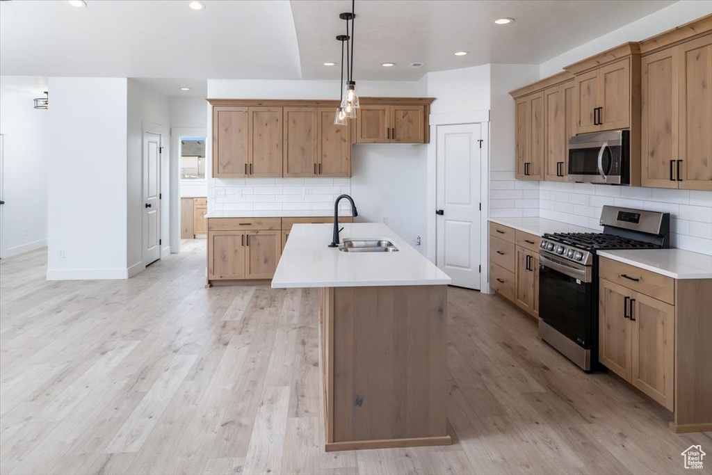 Kitchen with backsplash, light hardwood / wood-style floors, a kitchen island with sink, and appliances with stainless steel finishes