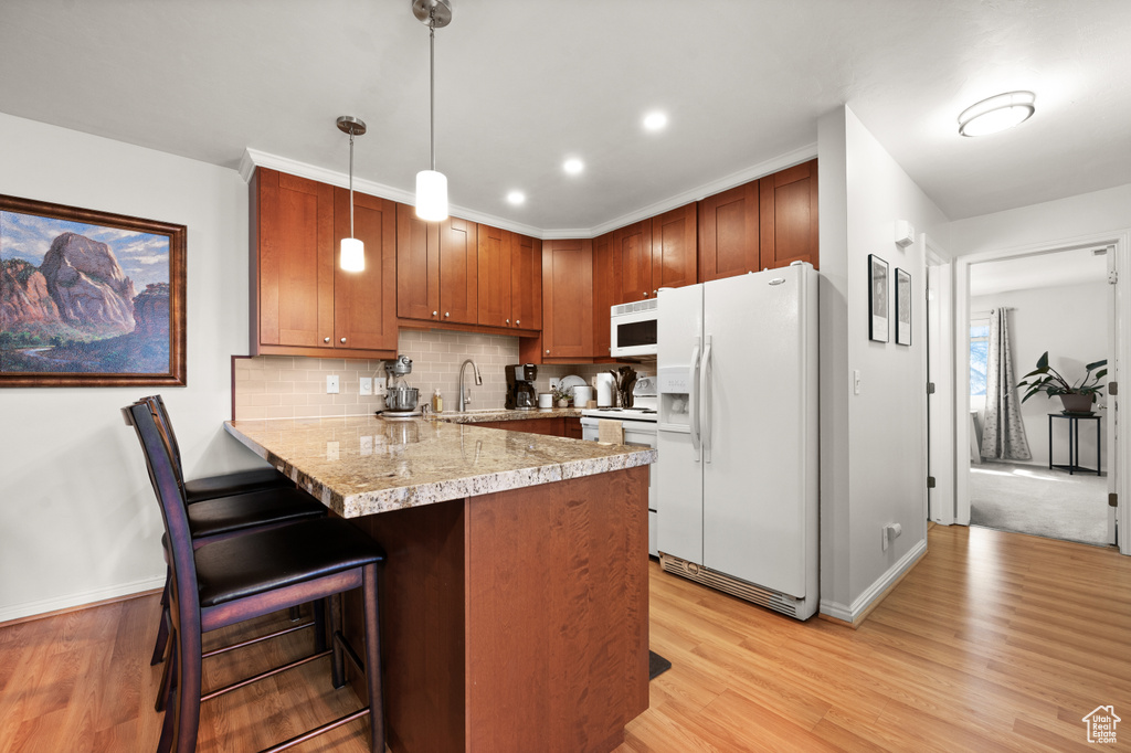 Kitchen with hanging light fixtures, white appliances, light hardwood / wood-style floors, a kitchen breakfast bar, and kitchen peninsula