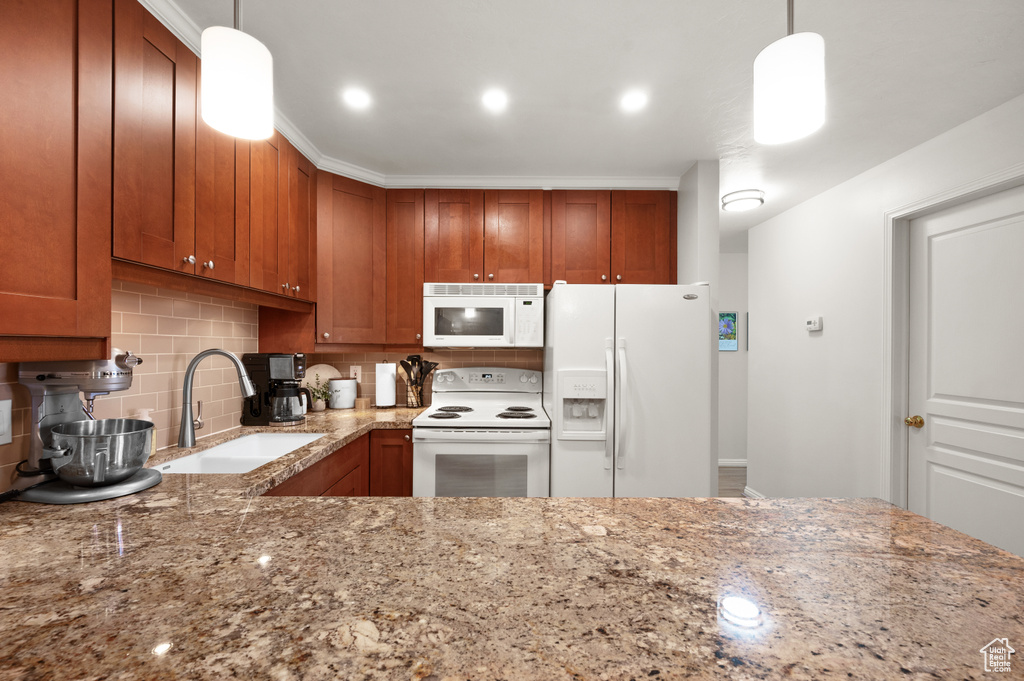Kitchen featuring light stone counters, white appliances, backsplash, decorative light fixtures, and sink