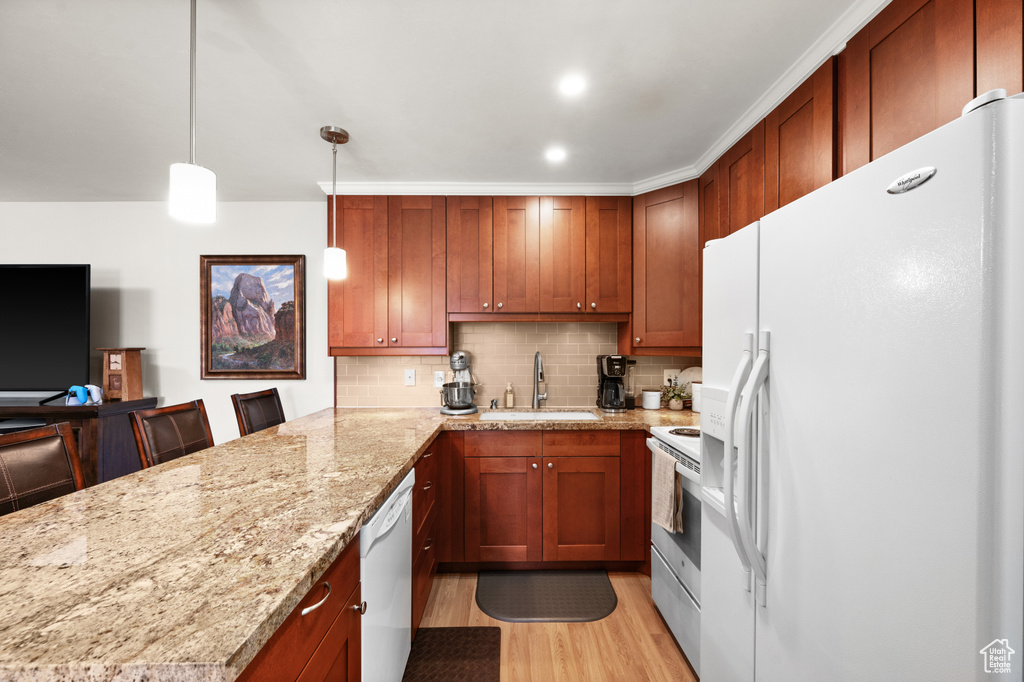 Kitchen with a breakfast bar, light hardwood / wood-style flooring, pendant lighting, backsplash, and white appliances
