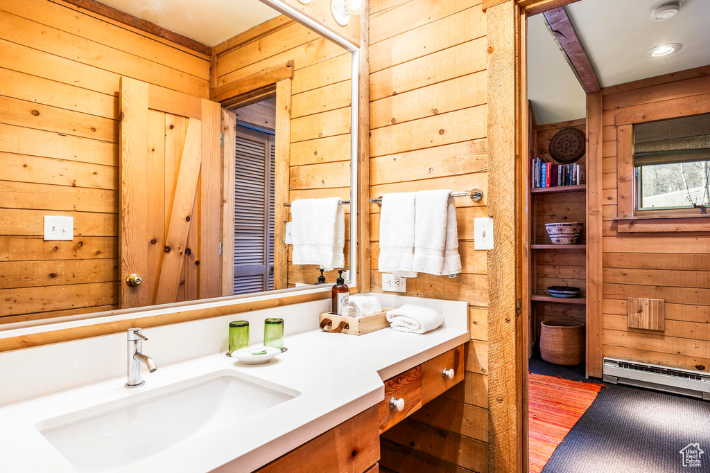 Bathroom featuring wooden walls, baseboard heating, and vanity with extensive cabinet space