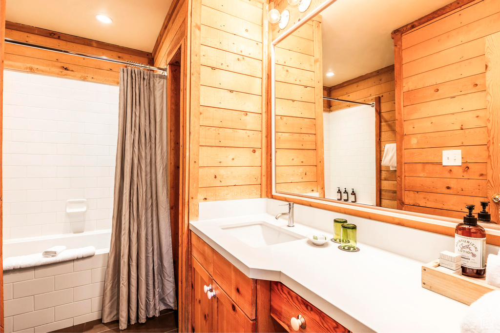 Bathroom featuring wooden walls, shower / bath combo with shower curtain, and vanity with extensive cabinet space