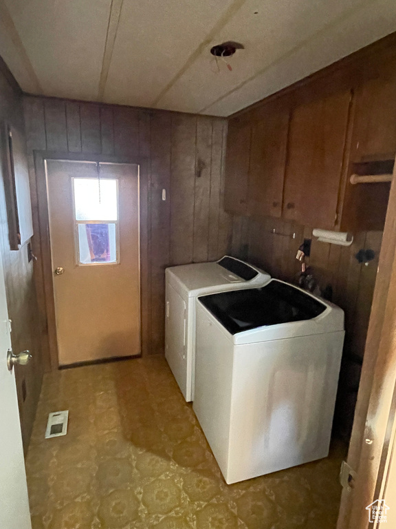Washroom with washing machine and clothes dryer, wood walls, and light tile flooring