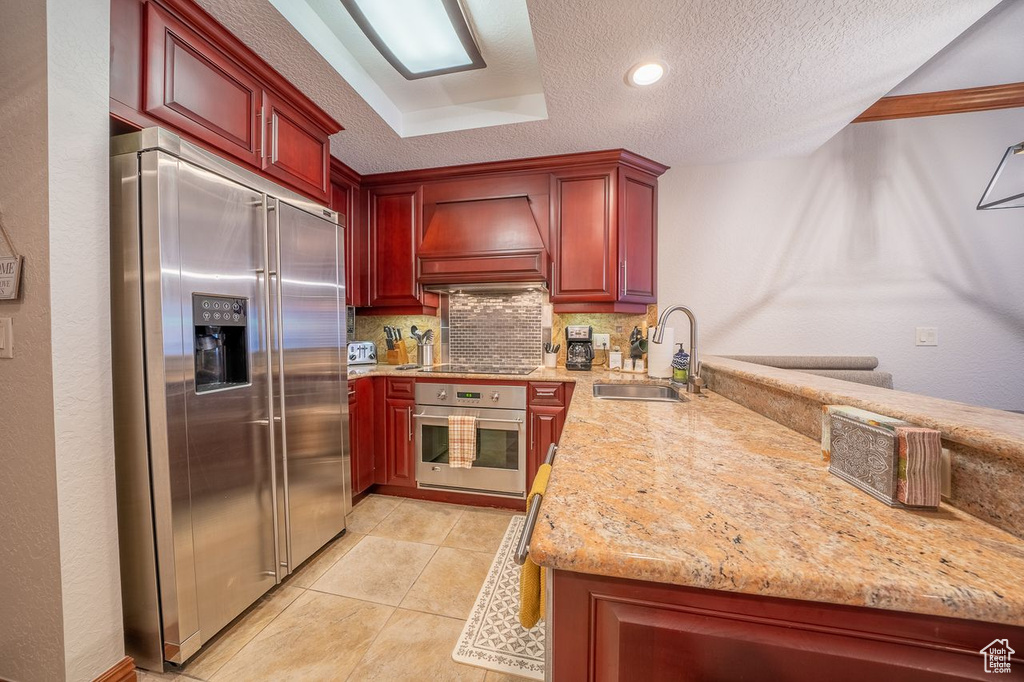 Kitchen with stainless steel appliances, light stone countertops, backsplash, premium range hood, and sink