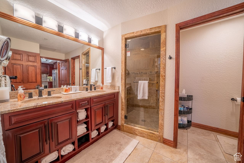 Bathroom featuring a shower with shower door, oversized vanity, double sink, a textured ceiling, and tile flooring