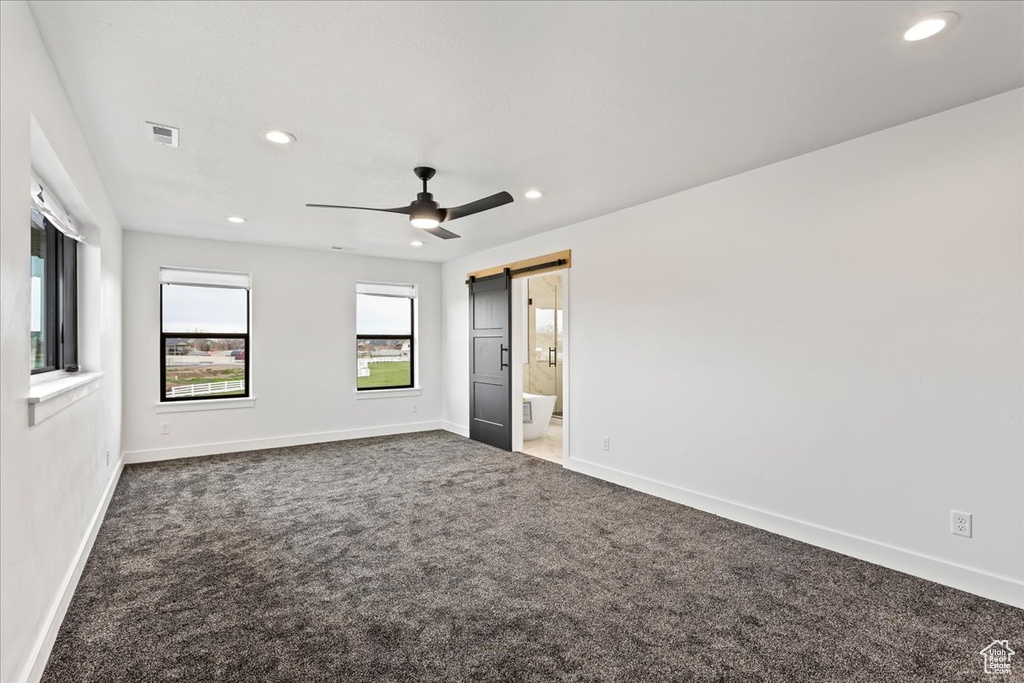 Carpeted empty room featuring a barn door and ceiling fan