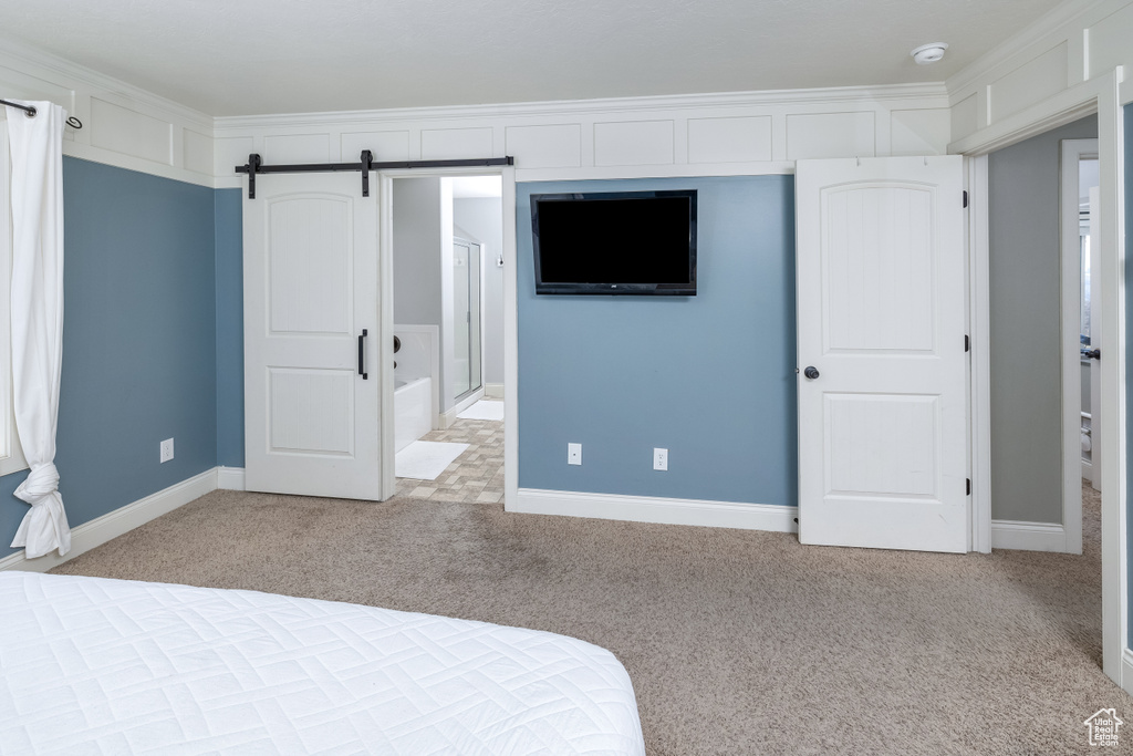 Unfurnished bedroom with a barn door, ornamental molding, and light carpet