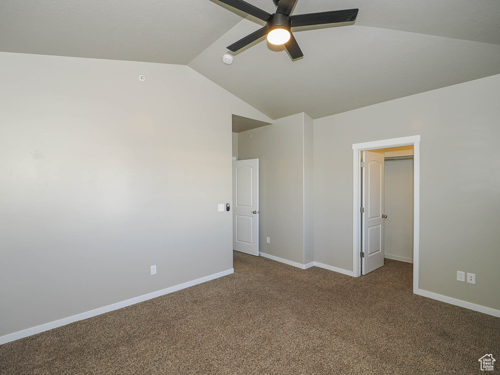 Unfurnished bedroom with ceiling fan, dark carpet, and lofted ceiling