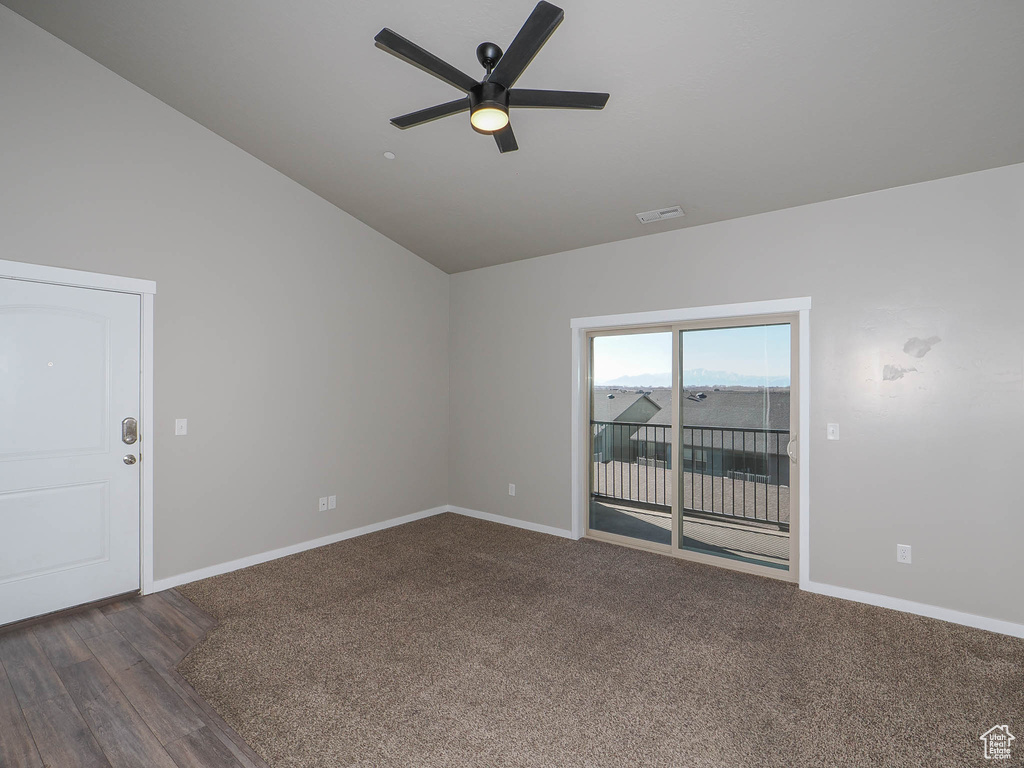 Empty room with vaulted ceiling, ceiling fan, and dark colored carpet