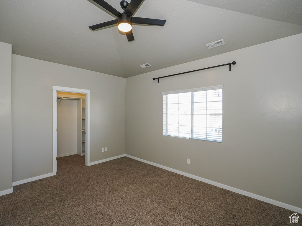 Carpeted empty room featuring ceiling fan and vaulted ceiling