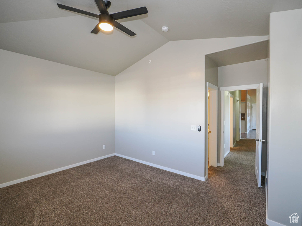 Spare room with dark colored carpet, vaulted ceiling, and ceiling fan