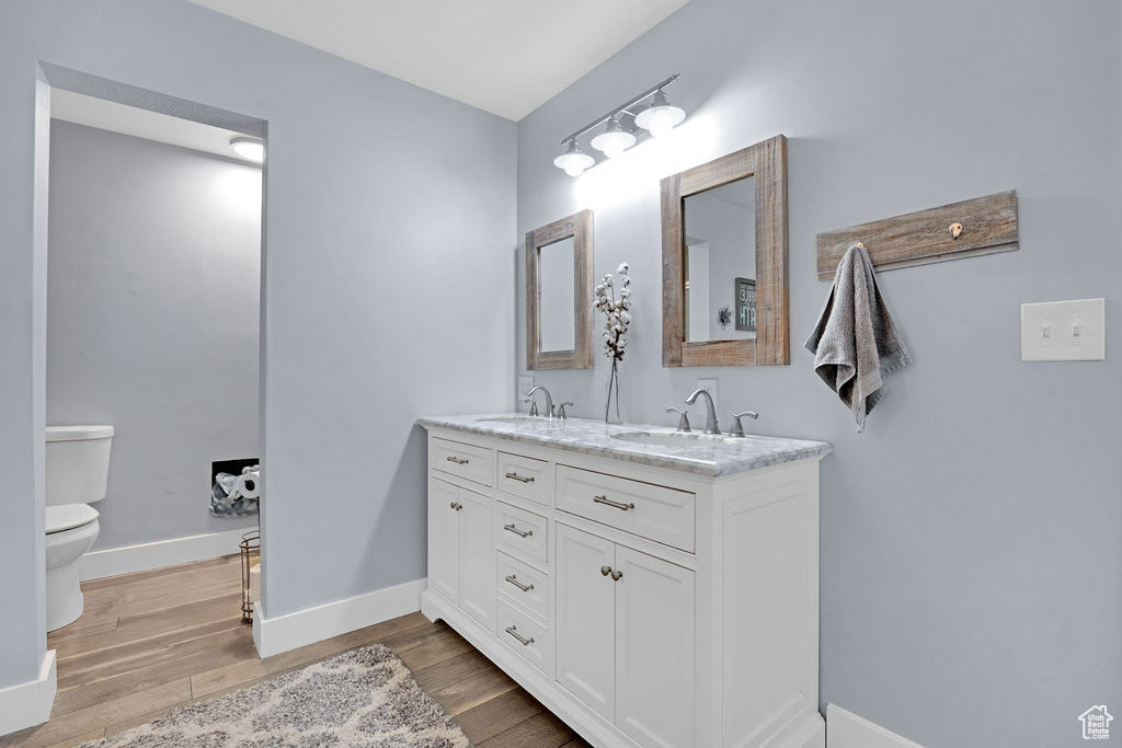 Bathroom with double sink vanity, toilet, and wood-type flooring