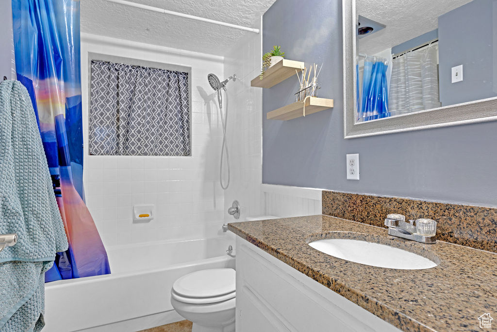 Full bathroom with shower / bath combination with curtain, a textured ceiling, vanity with extensive cabinet space, and toilet