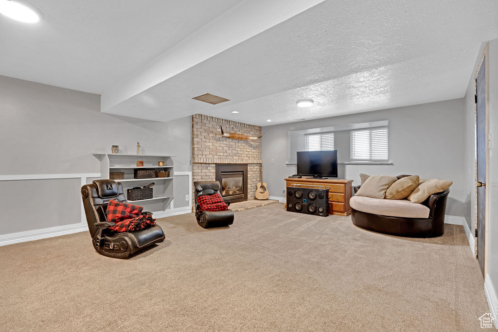 Carpeted living room with a fireplace, a textured ceiling, and brick wall