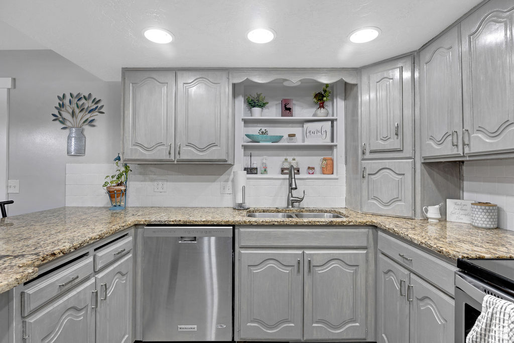 Kitchen featuring sink, gray cabinetry, stainless steel dishwasher, light stone countertops, and tasteful backsplash