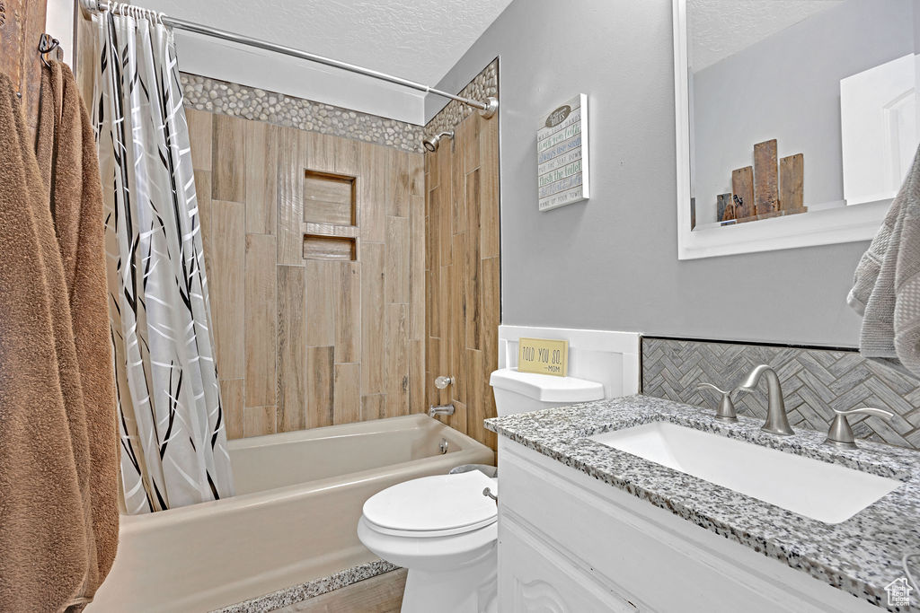 Full bathroom with toilet, large vanity, shower / bathtub combination with curtain, and a textured ceiling