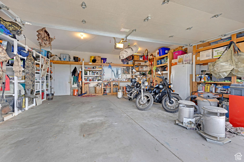Garage featuring a workshop area, white fridge, and a garage door opener