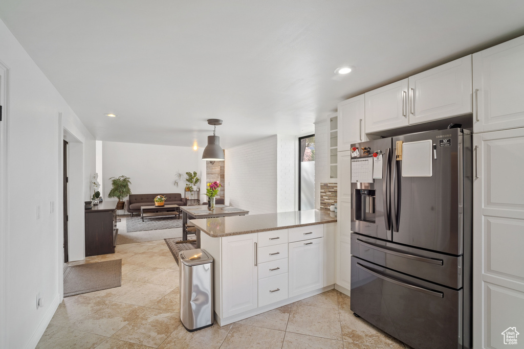 Kitchen featuring kitchen peninsula, white cabinetry, hanging light fixtures, stainless steel fridge, and light tile flooring