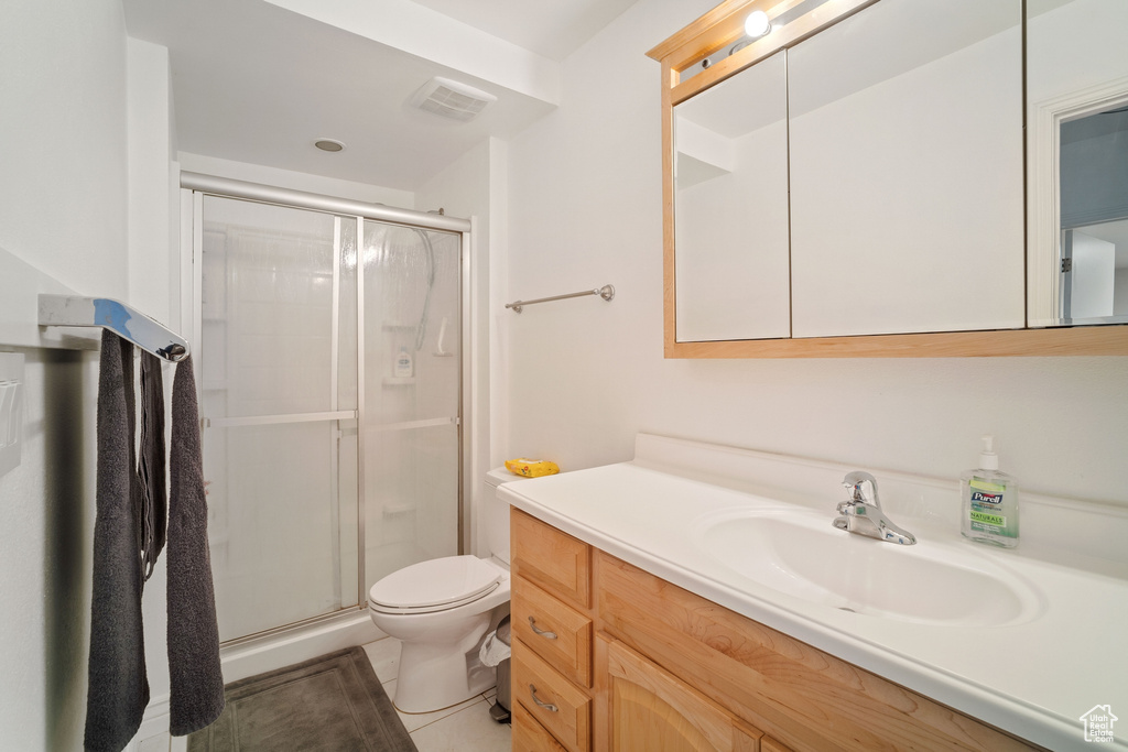 Bathroom featuring a shower with shower door, oversized vanity, toilet, and tile floors