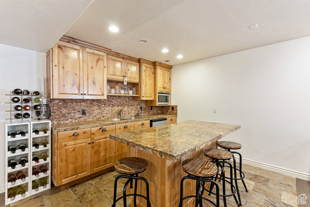 Kitchen featuring sink, light tile floors, a kitchen breakfast bar, dishwasher, and tasteful backsplash