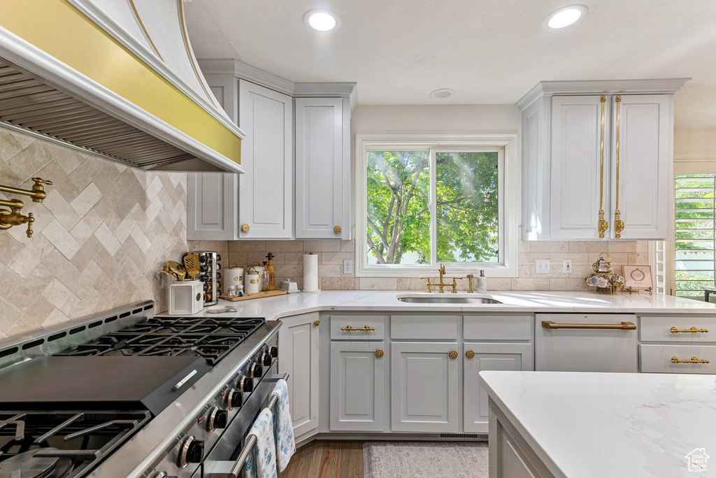 Kitchen with range with two ovens, premium range hood, backsplash, and a healthy amount of sunlight